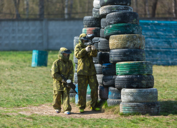 Boy in the camouflage holds a paintball gun  in one hand and protective helmet , standing on the field. sport lifestyle concept  - Photo, Image