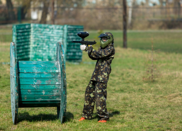 Niño en el camuflaje sostiene una pistola de paintball en una mano y casco protector, de pie en el campo. concepto de estilo de vida deportivo
  - Foto, imagen