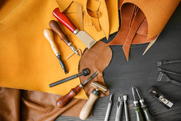 Cuero con herramientas artesanales sobre fondo de madera oscura
 - Foto, imagen