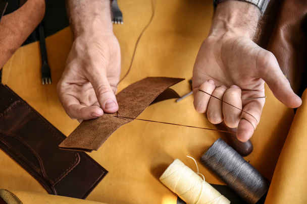 Hombre con aguja cosiendo cuero en taller
 - Foto, Imagen