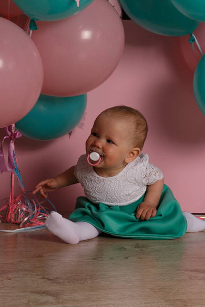 little girl in blue and white dress next to balloons, smiling, holiday, year, birthday child.sits on the floor a vortex of a pacifier - Foto, Imagen