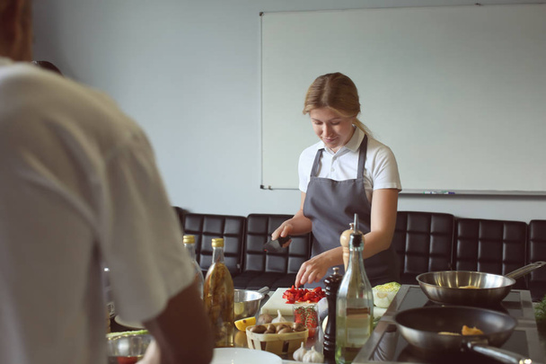 Jonge vrouw koken in de keuken van restaurant tijdens kooklessen - Foto, afbeelding