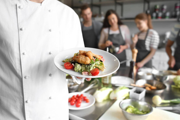 Чоловічий шеф-кухар тримає тарілку з підготовленою стравою під час уроків приготування їжі
 - Фото, зображення