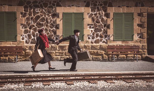 Pareja joven con maleta vintage corriendo rápido fuera de una estación de tren para coger el último tren para el viaje
. - Foto, Imagen