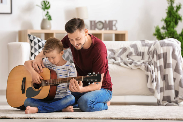 Isä opettaa poikaansa soittamaan kitaraa kotona.
 - Valokuva, kuva