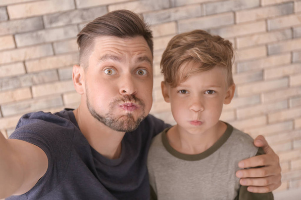 Little boy with his dad taking selfie on brick wall background - Foto, Imagen