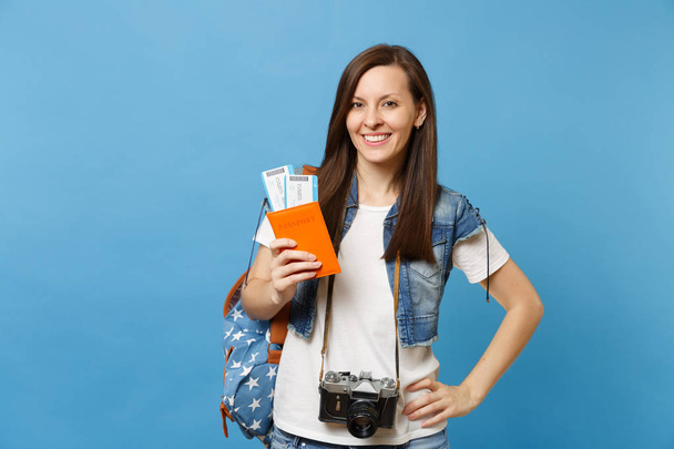 junge lächelnde Studentin mit Rucksack und Retro-Vintage-Fotokamera am Hals, die auf blauem Hintergrund isoliert die Bordkarten für Reisepässe hält. Ausbildung an Universitäten im Ausland. Flugreise - Foto, Bild