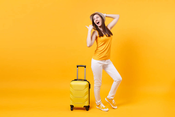 旅行観光女性夏カジュアルな服を着て、黄色オレンジ色の背景に分離されたスーツケースと帽子。女性の乗客は、週末の息抜きに旅行に海外旅行します。空気飛行の旅のコンセプト - 写真・画像