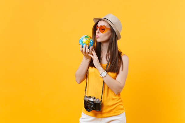 Toeristische vrouw in zomer casual kleding, hoed op zoek en zoenen globe geïsoleerd op geel oranje achtergrond. Passagier reizen in het buitenland te reizen op weekend uitje. Air vlucht reis keuze concept - Foto, afbeelding