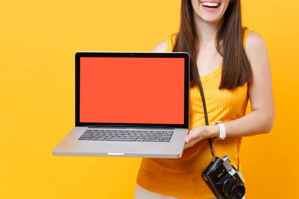 Mulher turística cortada segurando laptop pc computador com tela vazia preta em branco isolado no fundo laranja amarelo. Mulher viajando para o exterior para viajar nos fins de semana de fuga. Conceito de viagem aérea
 - Foto, Imagem