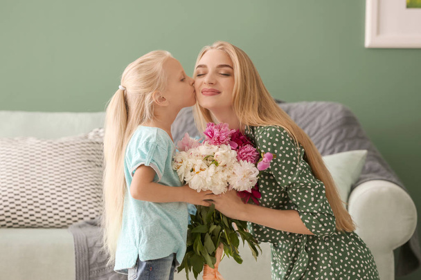 Attractive young woman and her cute little daughter with beautiful flowers at home - Photo, image