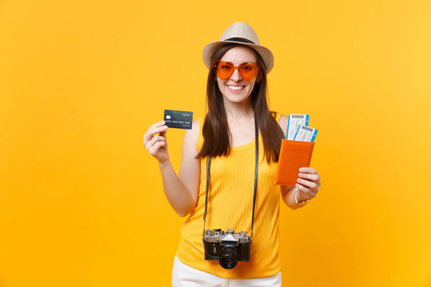Mujer turista feliz en ropa casual de verano, sombrero con tarjeta de crédito, pasaportes aislados sobre fondo amarillo anaranjado. Mujer viajando al extranjero para viajar los fines de semana de escapada. Concepto de vuelo aéreo
 - Foto, imagen