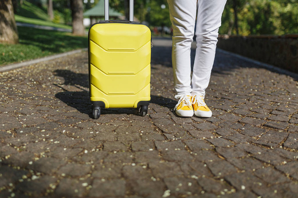 Rajattu ammuttu jalat keltainen lenkkarit, turisti nainen rento vaatteita matkalaukku seisoo, kävely kaupungin ulkona. Tyttö matkustaa ulkomaille viikonloppumatkalle. Matkailuelämäntapa
 - Valokuva, kuva