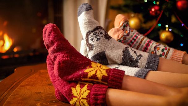 Famille en chaussettes de laine tenant les pieds sur une table en bois à côté d'une cheminée et d'un sapin de Noël
 - Photo, image