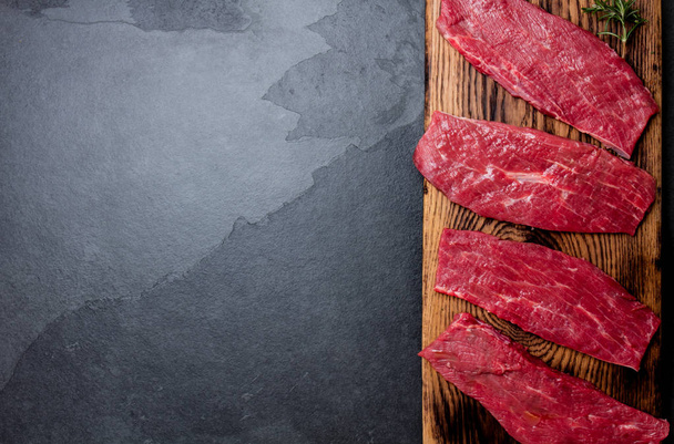 Fresh raw meat beef steaks. Beef tenderloin on wooden board, spices, herbs, oil on slate gray background. Food background with copy space. - Foto, imagen