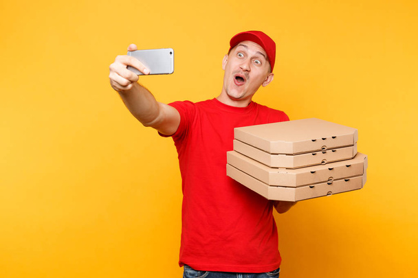Człowiek dostawy w Czerwonym Kapturku t-shirt żywności zamówienia włoska pizza w flatbox puste pola na żółtym tle. Kurier ' Pizzaman ' mężczyzna pracownik robi biorąc selfie zrzut na telefon komórkowy. Pojęcie usługi - Zdjęcie, obraz