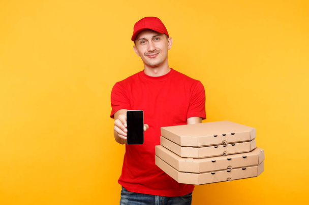 Delivery man in red cap t-shirt giving food order italian pizza in flatbox boxes on yellow background. Male employee pizzaman courier hold mobile phone with blank empty screen mockup. Service concept - Valokuva, kuva
