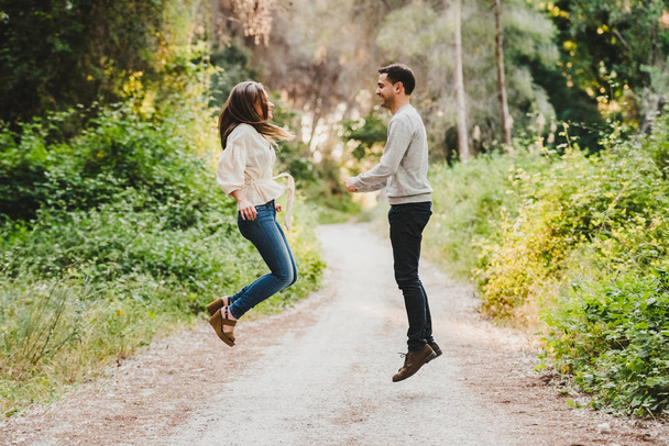 couple jumping and laughing in the middle of the green road - Photo, Image