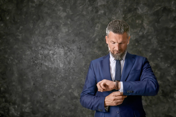 Hombre maduro guapo en traje elegante con reloj de pulsera sobre fondo de textura oscura
 - Foto, Imagen