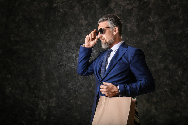 ダーク テクスチャ背景のショッピング バッグとスーツでハンサムな中年の男性 - 写真・画像
