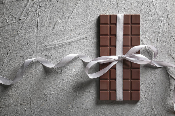 Tasty milk chocolate bar with ribbon on textured background - Photo, Image