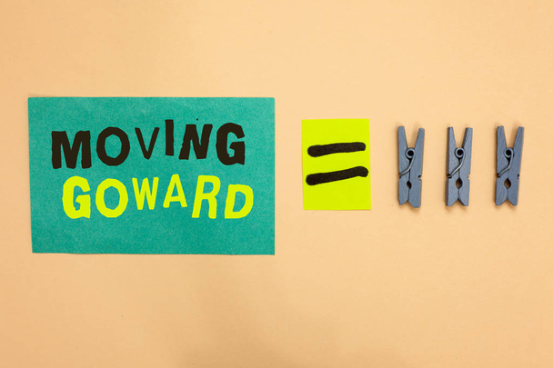 Handwriting text Moving Goward. Concept meaning Towards a Point Move on Going Ahead Further Advance Progress Turquoise paper reminder equal sign several clothespins sending message. - Photo, Image