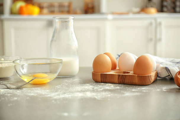 Wooden holder with chicken eggs and ingredients for preparing pastry on kitchen table - Φωτογραφία, εικόνα