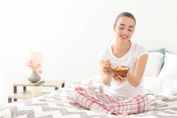 Beautiful young woman eating tasty oatmeal for breakfast in bedroom - Valokuva, kuva
