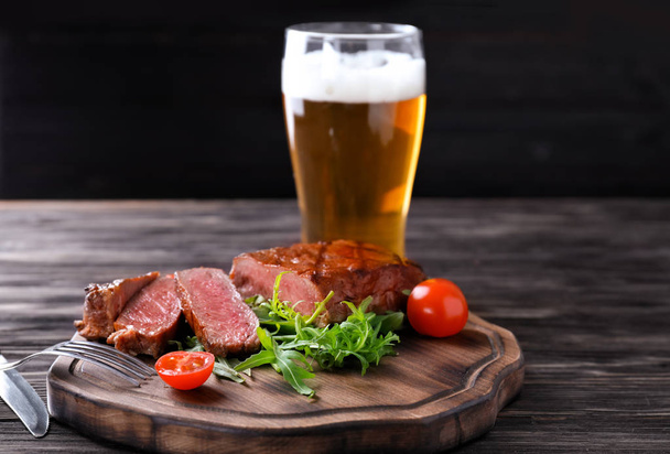 Dřevěná deska s chutné grilované steaky a pivo na stole - Fotografie, Obrázek
