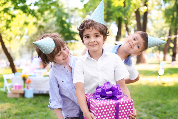 Ładny chłopczyk z pudełko i jego przyjaciół na przyjęcie urodzinowe na zewnątrz - Zdjęcie, obraz