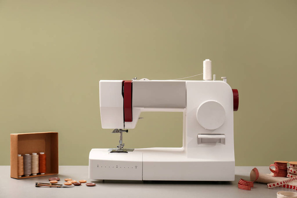 Modern sewing machine with tailor's supplies on table against color background - Фото, изображение