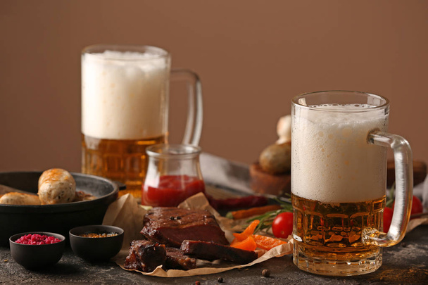Mugs of delicious beer, grilled steak and  sausages on grunge table - Photo, image