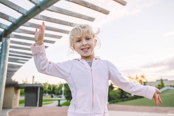 Boldog gyermekkor. Aranyos aranyos kis szőke kaukázusi lány gyermek vicces ostoba pofákat portréja. Gyerek játék, szórakozás park kívül a naplemente. Tónusú film szűrőkkel.  - Fotó, kép