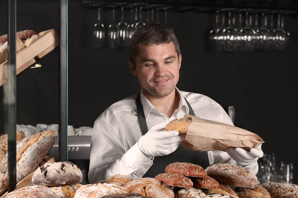 Hombre guapo con pan recién horneado trabajando en panadería
 - Foto, Imagen