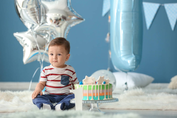 Cute little boy with birthday cake sitting on fluffy rug in room - Foto, afbeelding