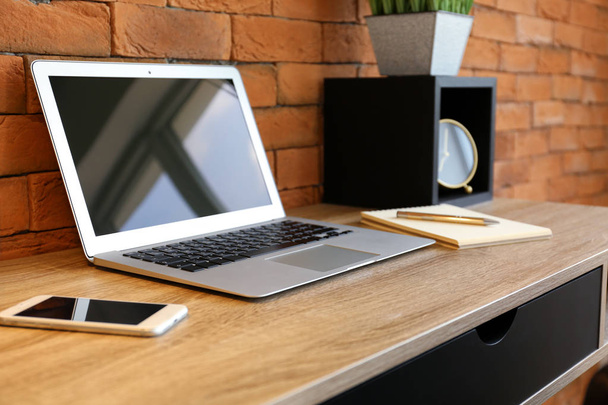 Modern laptop-val mozgatható telefon, a fából készült asztal közelében téglafal hivatalban - Fotó, kép