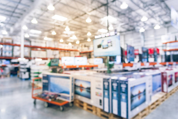 Blurred TVs shopping at wholesale club. Television retail shop, row of big screen, smart TVs display on shelves and on flatbed cart. Defocused large warehouse interior technology aisle bokeh light. - Photo, Image
