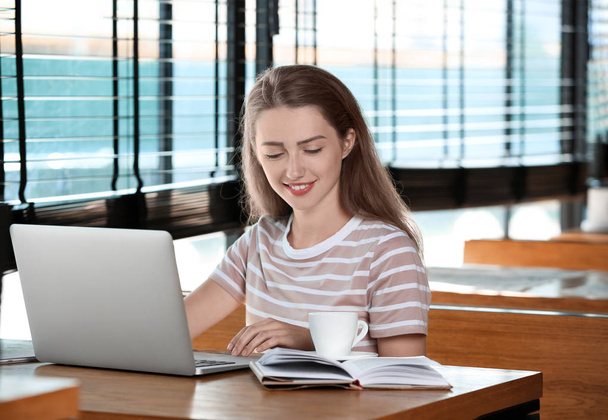 Jeune femme pigiste avec ordinateur portable travaillant dans un café
 - Photo, image