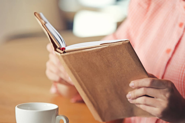 Jonge vrouw leesboek in café, close-up - Foto, afbeelding