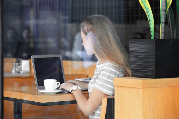 Mladé samice freelancer s notebookem pracovat v kavárně, zobrazit prostřednictvím skleněné okno - Fotografie, Obrázek