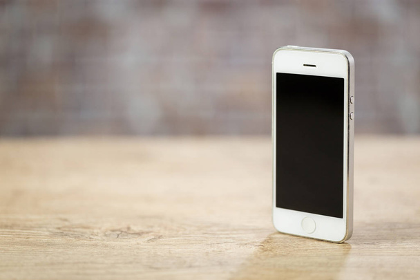 Smartphone standing on a wooden table in front of a brick wall. copy Space - Фото, изображение