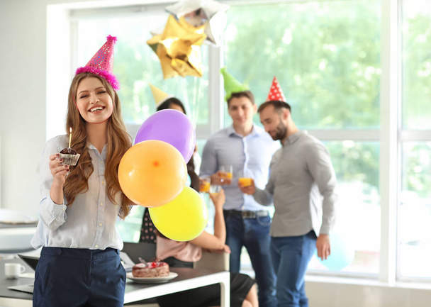 Mladá žena s chutné muffin a vzduchové bubliny na narozeninovou oslavu v úřadu - Fotografie, Obrázek