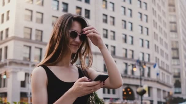 Amazing panning shot of excited Caucasian young tourist woman with smartphone in sunglasses looking around in New York. - Filmati, video