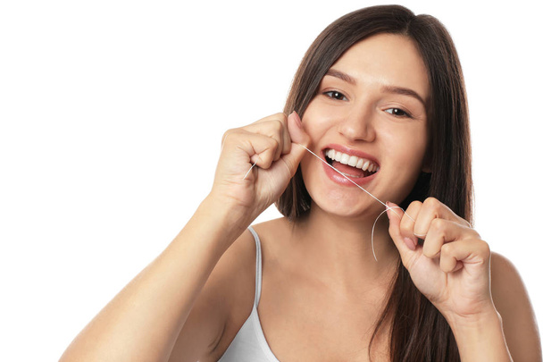 Νεαρή γυναίκα οδοντικό νήμα τα δόντια της σε άσπρο φόντο - Φωτογραφία, εικόνα