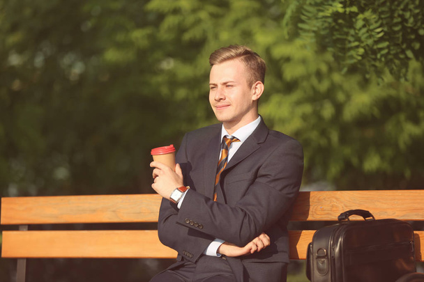Młody człowiek w ubrania formalne odpoczynku filiżankę kawy w parku na słoneczny dzień - Zdjęcie, obraz