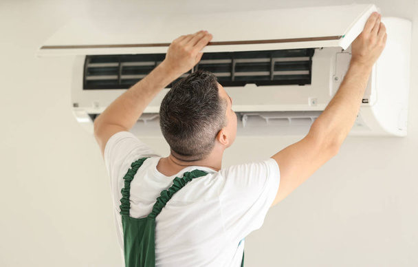 Sähköasentaja korjaamassa ilmastointilaitetta sisätiloissa
 - Valokuva, kuva