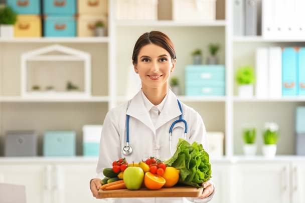 Nutricionista femenina con tabla con frutas y verduras frescas en su oficina
 - Foto, Imagen