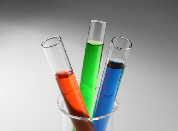 Δοκιμαστικοί σωλήνες με πολύχρωμα υγρά σε ποτήρι ζέσεως γυαλί επάνω ελαφρύς υπόβαθρο - Φωτογραφία, εικόνα