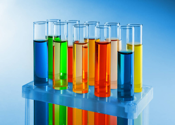 Reageerbuisjes met kleurrijke vloeistoffen in houder op lichte achtergrond - Foto, afbeelding