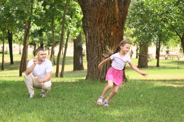 Happy father and daughter blowing soap bubbles in park - Fotó, kép